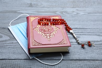 Photo of Muslim prayer beads, Quran and medical mask on grey wooden table