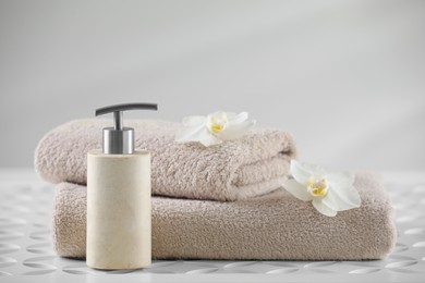 Photo of Soft folded towels, orchid flowers and dispenser on white table