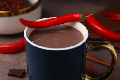 Cup of hot chocolate with chili pepper on grey table, closeup