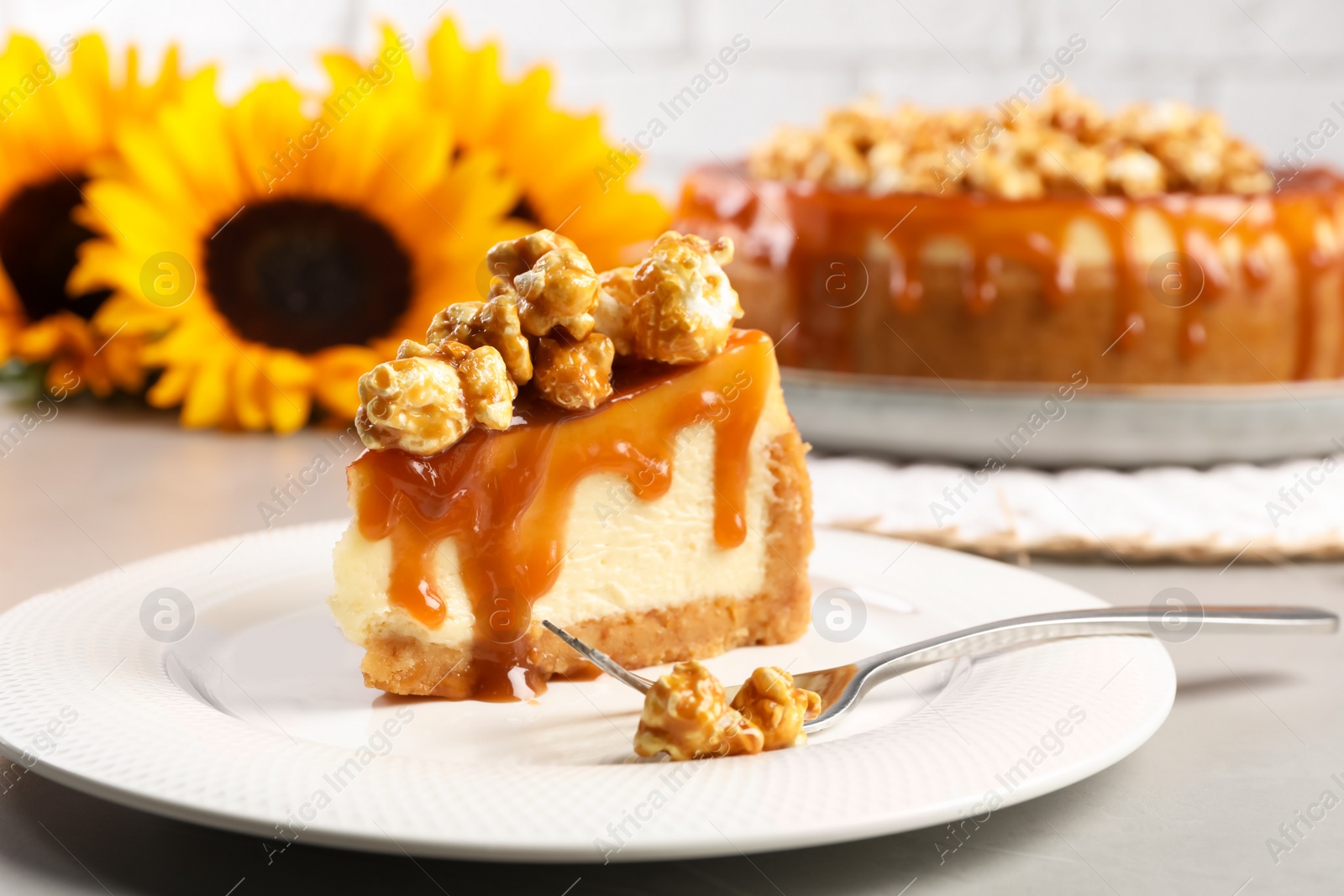 Photo of Piece of delicious caramel cheesecake with popcorn on light grey table, closeup