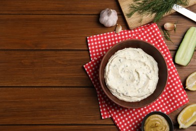 Photo of Delicious tartar sauce and ingredients on wooden table, flat lay. Space for text