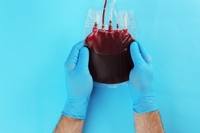 Doctor in gloves holding blood pack on color background, top view. Donation day