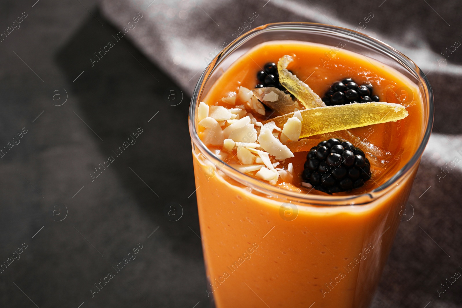 Photo of Glass of delicious smoothie with blackberries, candied mango and almond on grey table, closeup. Space for text