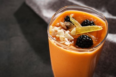 Glass of delicious smoothie with blackberries, candied mango and almond on grey table, closeup. Space for text