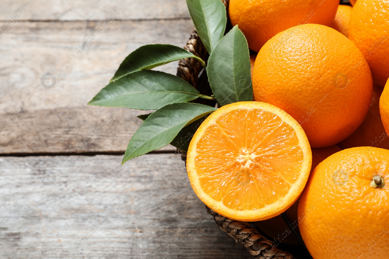 Photo of Wicker bowl with ripe oranges on wooden background, closeup. Space for text