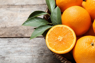 Wicker bowl with ripe oranges on wooden background, closeup. Space for text