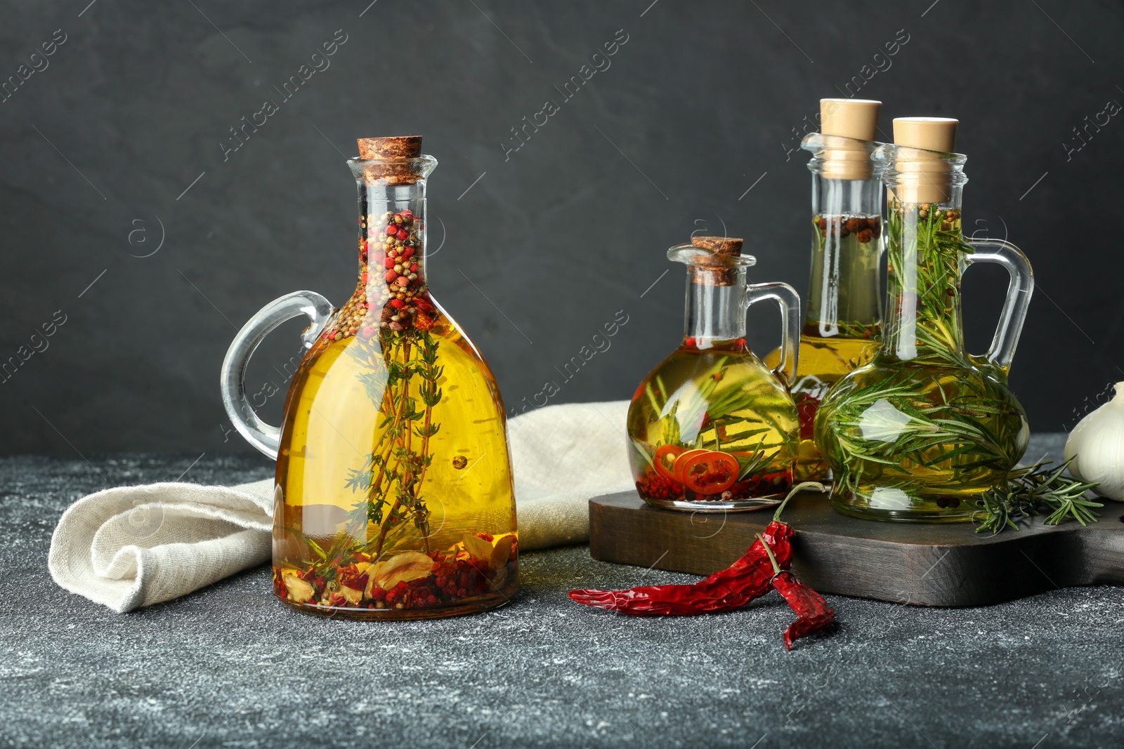 Photo of Cooking oil with different spices and herbs in jugs on light grey table