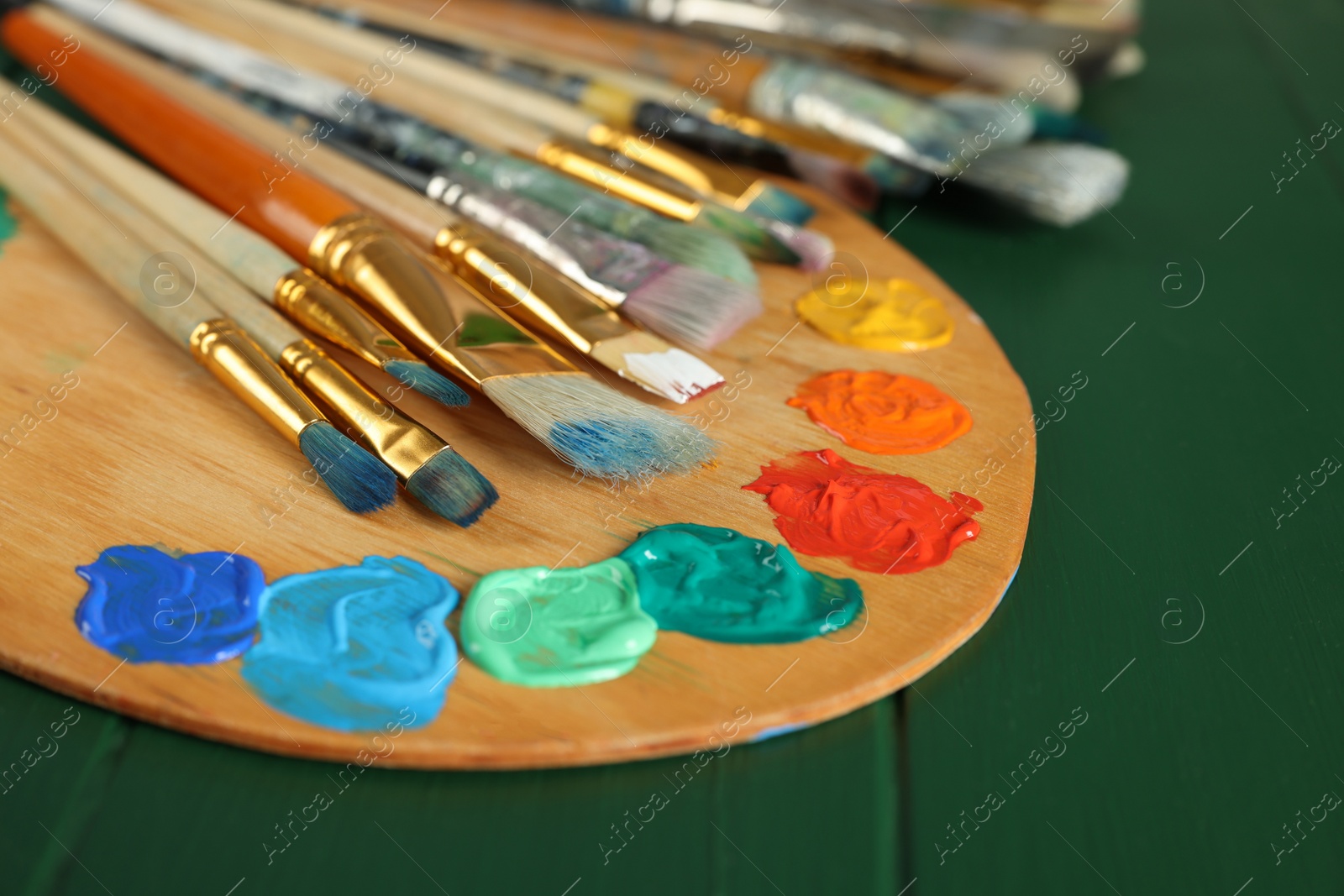 Photo of Many paintbrushes and palette on green wooden table, closeup