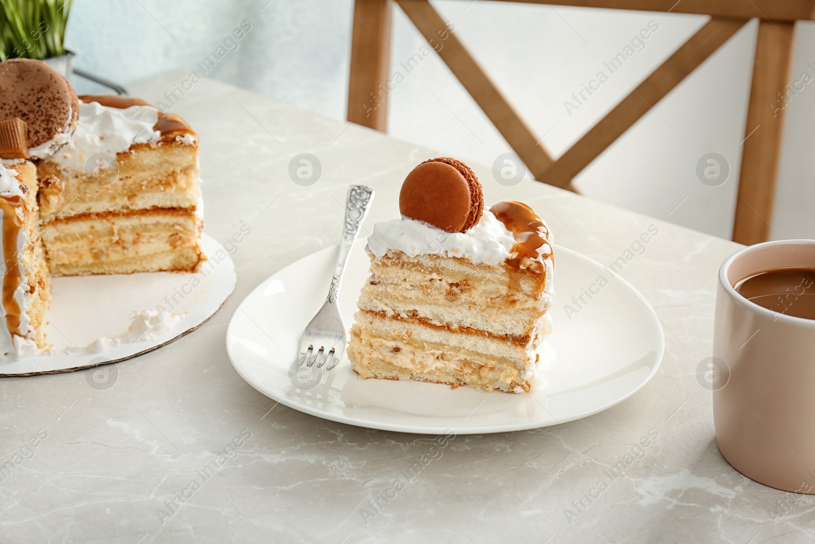 Photo of Piece of delicious homemade cake with caramel sauce and macaron on table