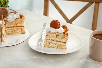 Piece of delicious homemade cake with caramel sauce and macaron on table