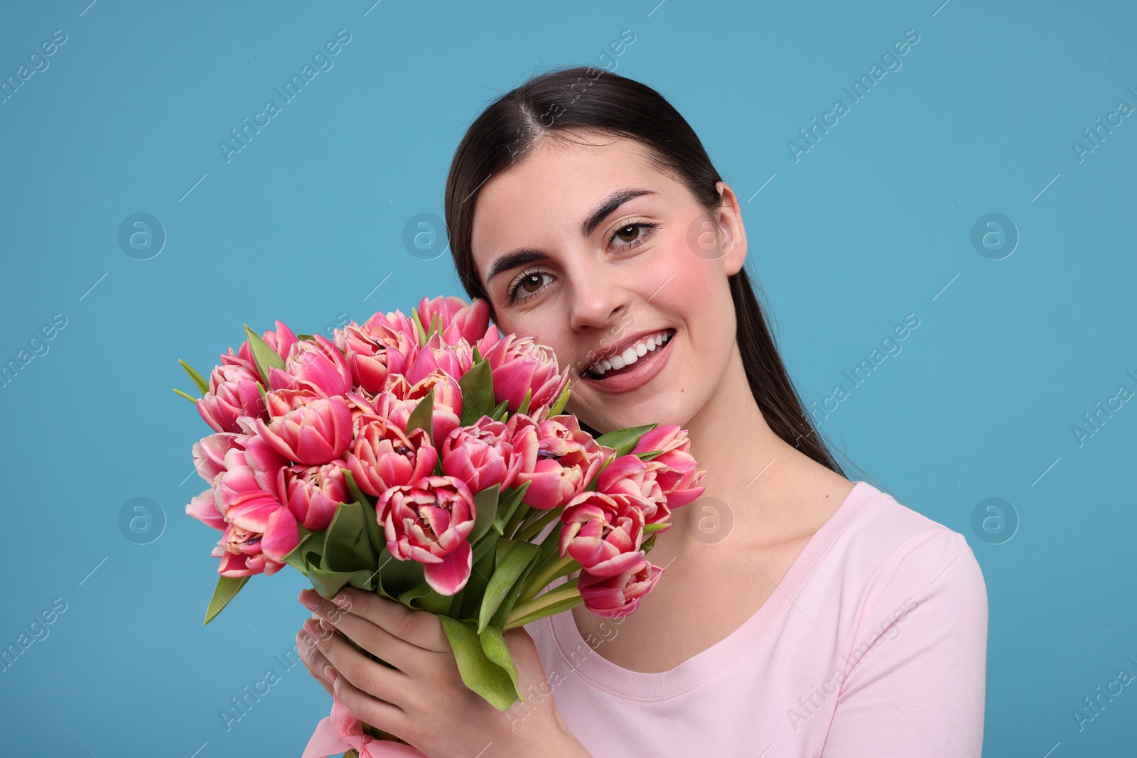 Photo of Happy young woman with beautiful bouquet on light blue background