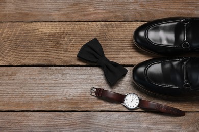 Stylish black bow tie, wristwatch and shoes on wooden background, flat lay. Space for text