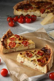 Photo of Pieces of delicious homemade quiche with prosciutto and tomatoes on light grey marble table