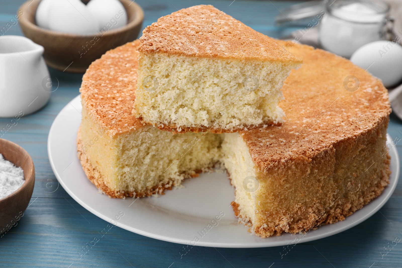 Photo of Tasty sponge cake and ingredients on light blue wooden table, closeup