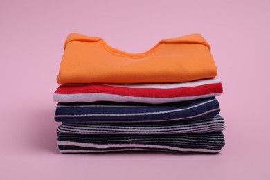 Stack of clean baby clothes on pink background