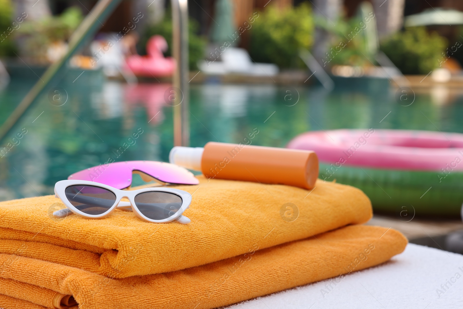 Photo of Beach towels, sunglasses and sunscreen on sun lounger near outdoor swimming pool at luxury resort