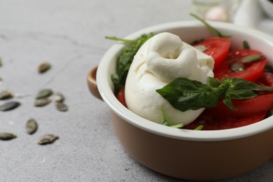 Delicious burrata cheese with tomatoes and pumpkin seeds on grey table, closeup. Space for text