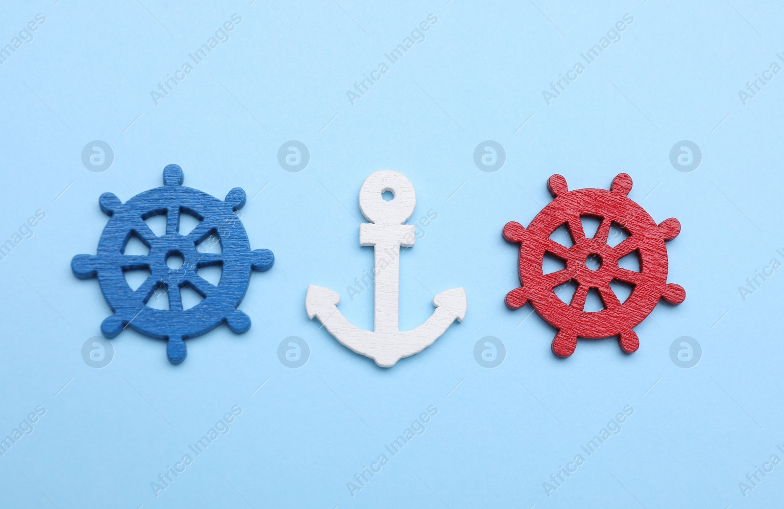 Photo of Anchor and ship wheel figures on pale blue background, flat lay