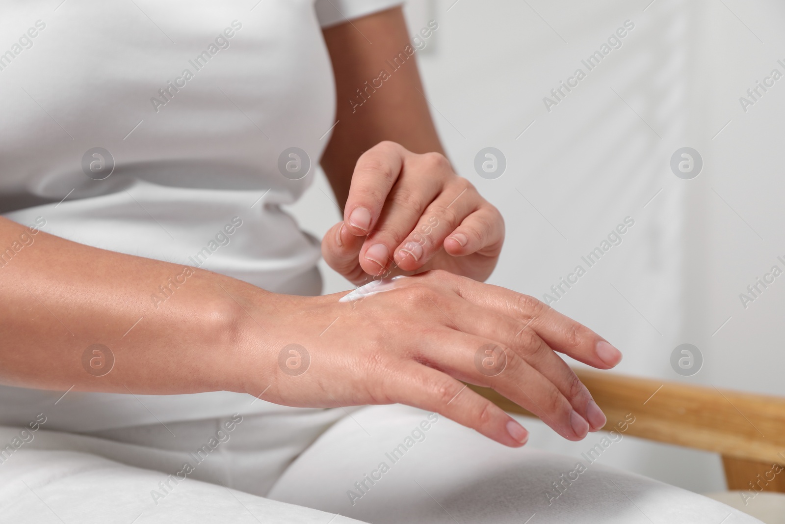 Photo of Woman applying cosmetic cream onto hand on blurred background, closeup