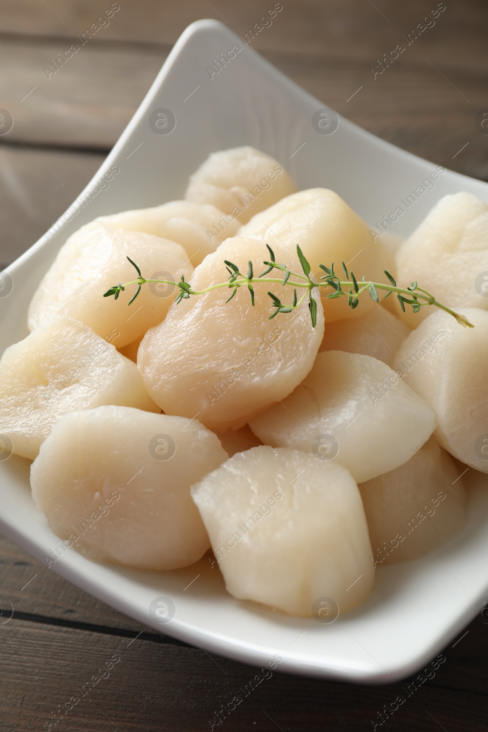 Photo of Fresh raw scallops and thyme in bowl on wooden table, closeup