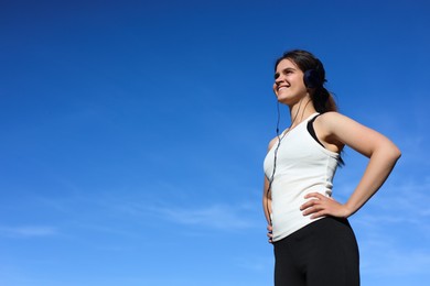 Woman listening to music against blue sky in morning, low angle view. Space for text