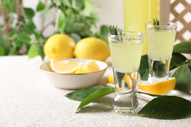 Photo of Tasty limoncello liqueur, lemons and green leaves on white textured table, closeup. Space for text