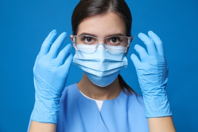 Photo of Doctor in protective mask, medical gloves and glasses against blue background