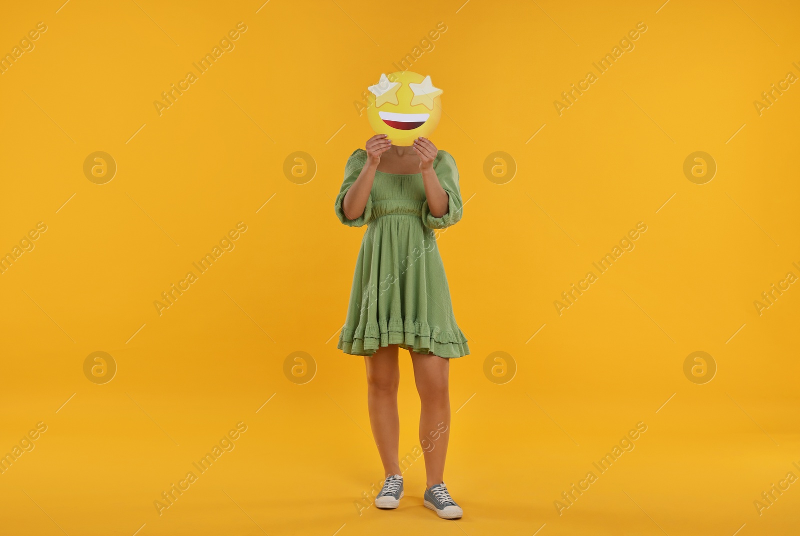 Photo of Woman holding emoticon with stars instead of eyes on yellow background