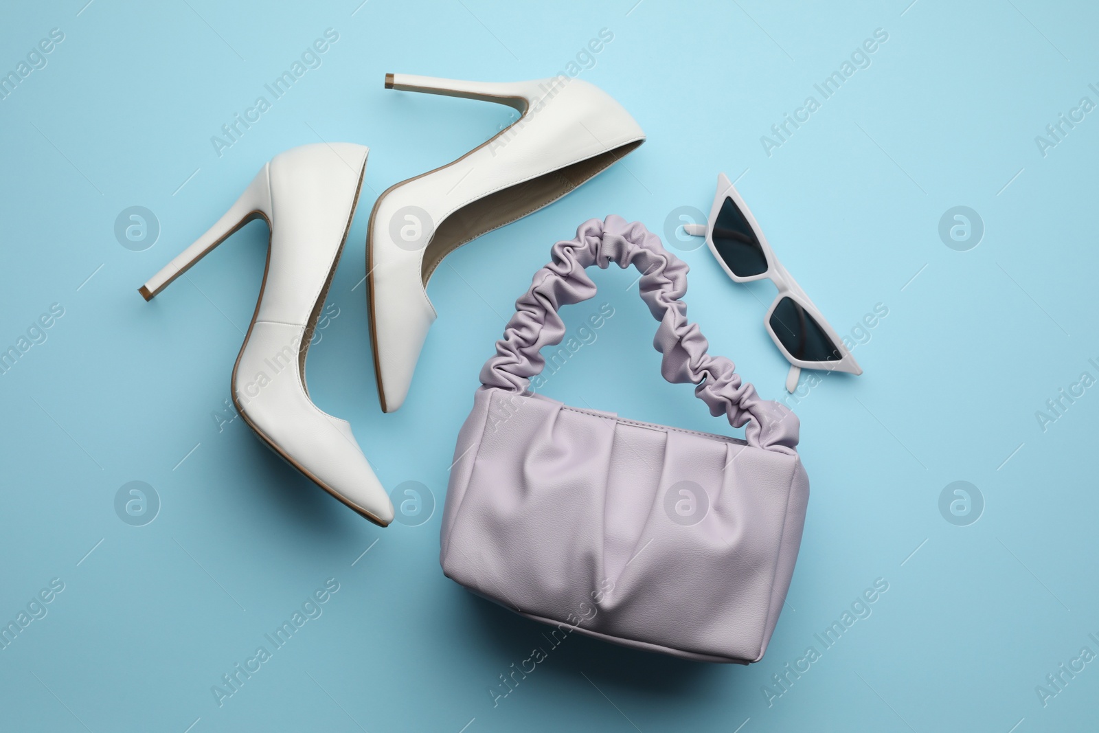 Photo of Stylish woman's bag, shoes and sunglasses on light blue background, flat lay