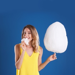 Photo of Happy young woman eating cotton candy on blue background