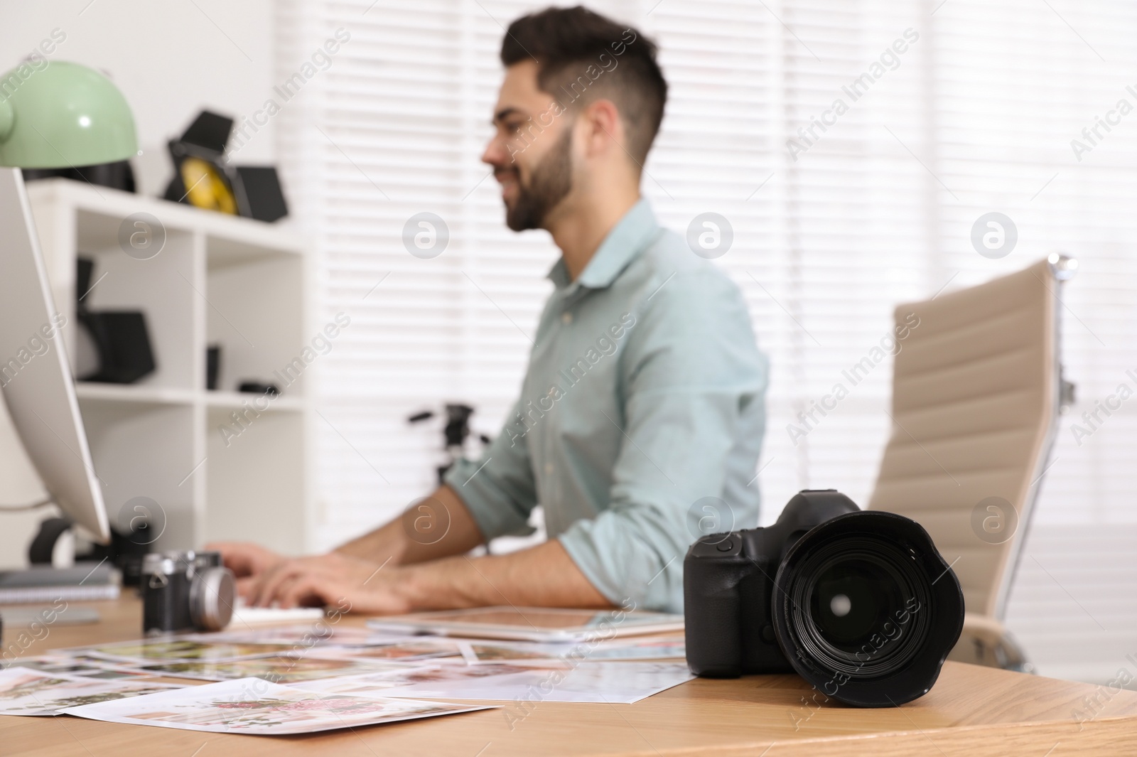 Photo of Professional photographer working at table in office, focus on camera