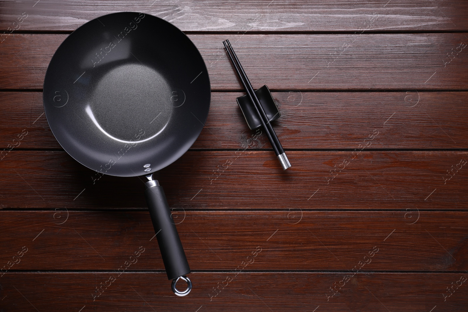 Photo of Empty iron wok and chopsticks on wooden table, flat lay. Space for text