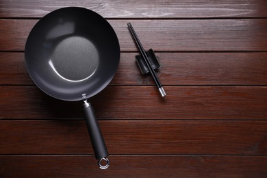 Empty iron wok and chopsticks on wooden table, flat lay. Space for text