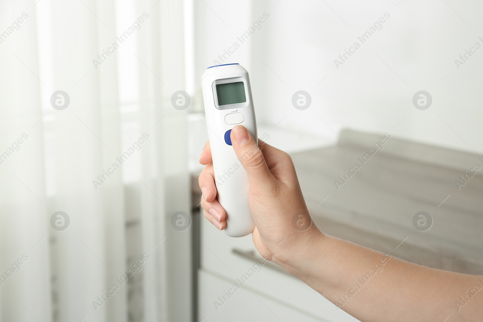 Photo of Woman with non contact infrared thermometer indoors, closeup