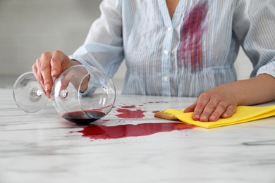Photo of Woman with stain on her shirt cleaning spilled wine from white marble table indoors, closeup