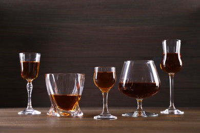 Different delicious liqueurs in glasses on wooden table