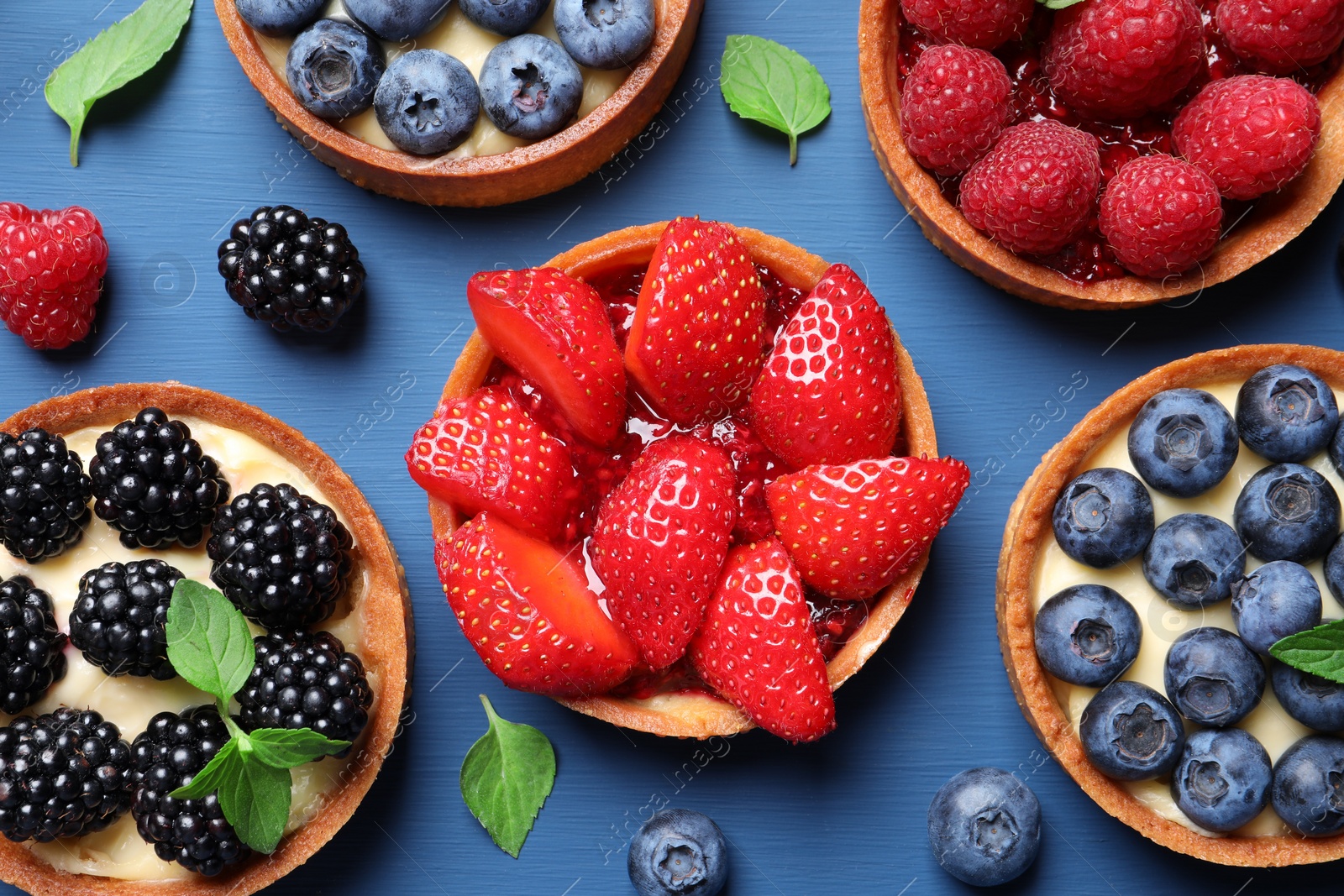 Photo of Tartlets with different fresh berries on blue wooden table, flat lay. Delicious dessert