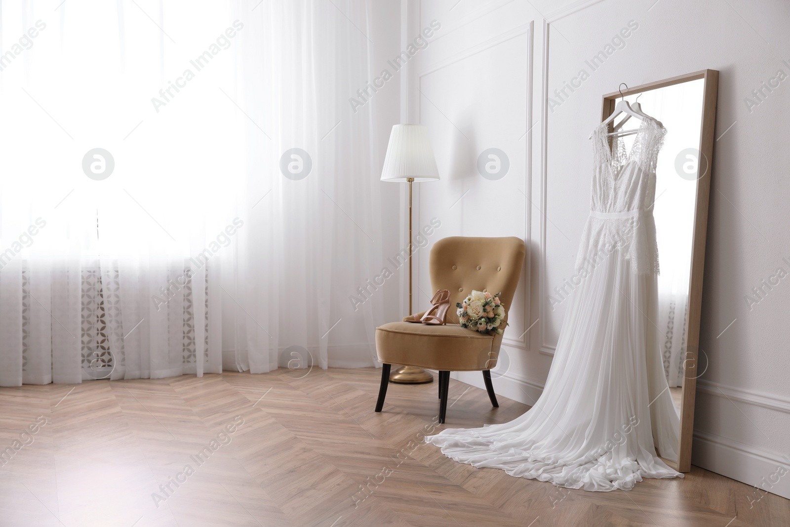 Photo of Elegant wedding dress hanging on large mirror in room