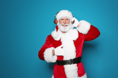 Photo of Santa Claus listening to Christmas music on color background