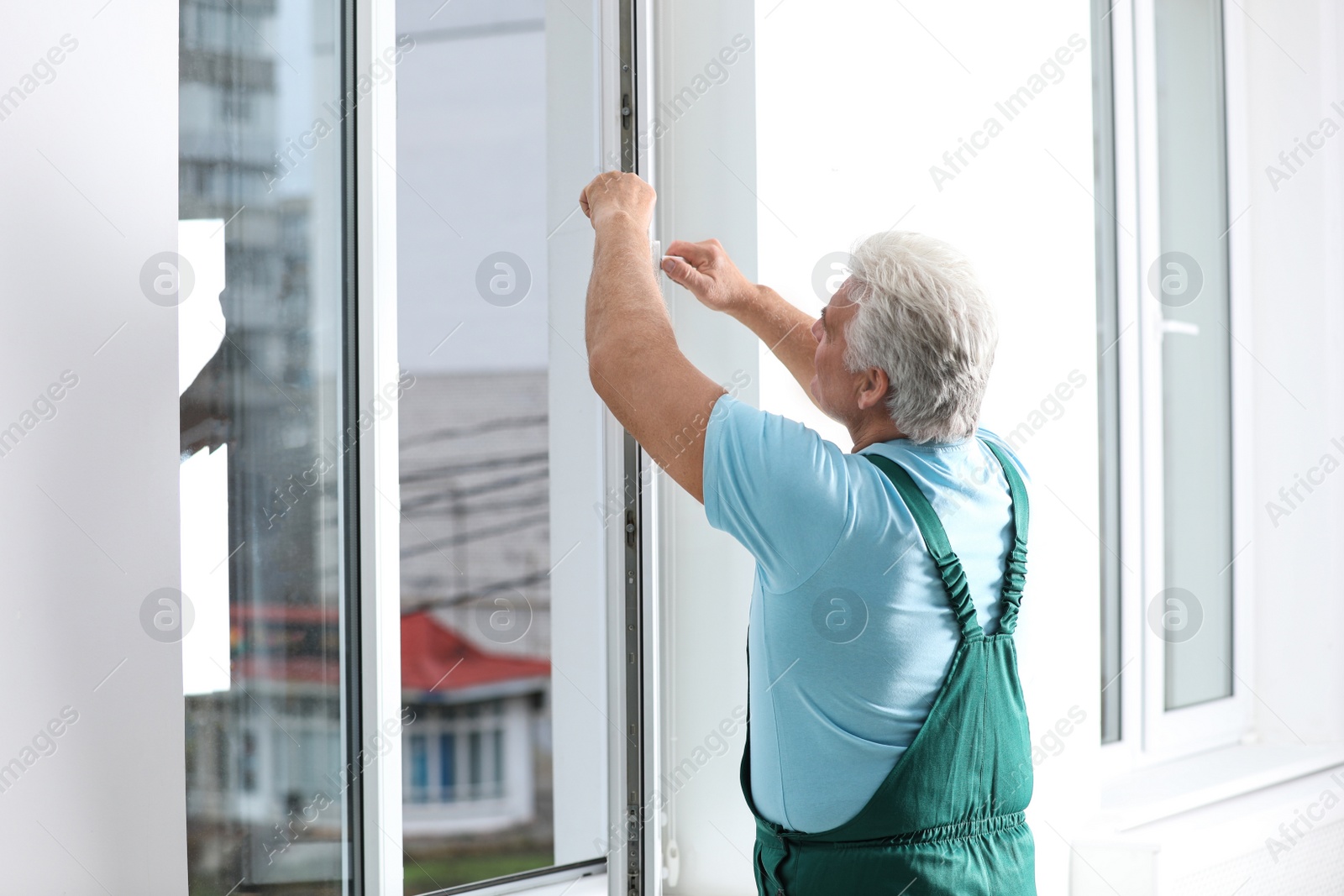 Photo of Mature construction worker repairing plastic window indoors