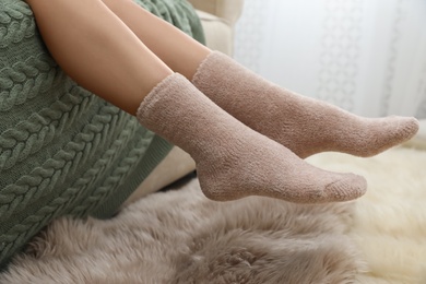 Photo of Woman in warm socks on sofa with knitted plaid, closeup