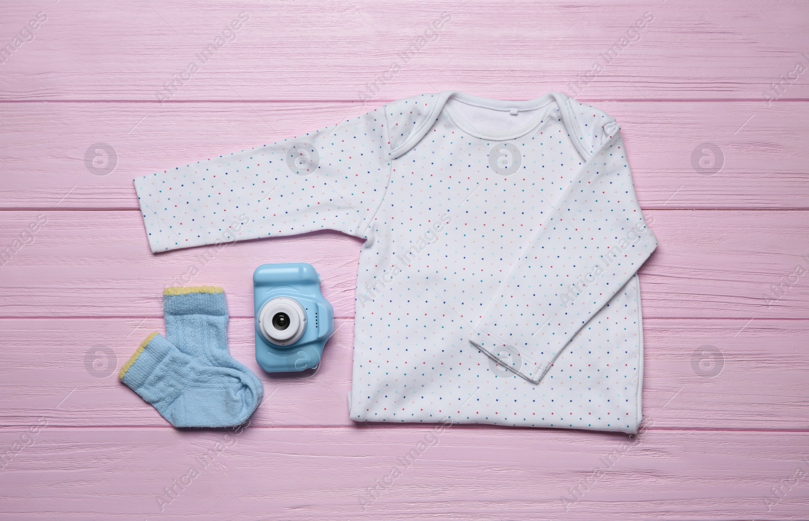 Photo of Baby clothes and camera on pink wooden background, flat lay