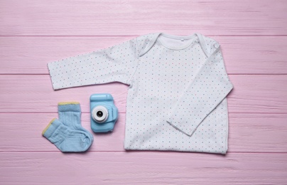 Photo of Baby clothes and camera on pink wooden background, flat lay