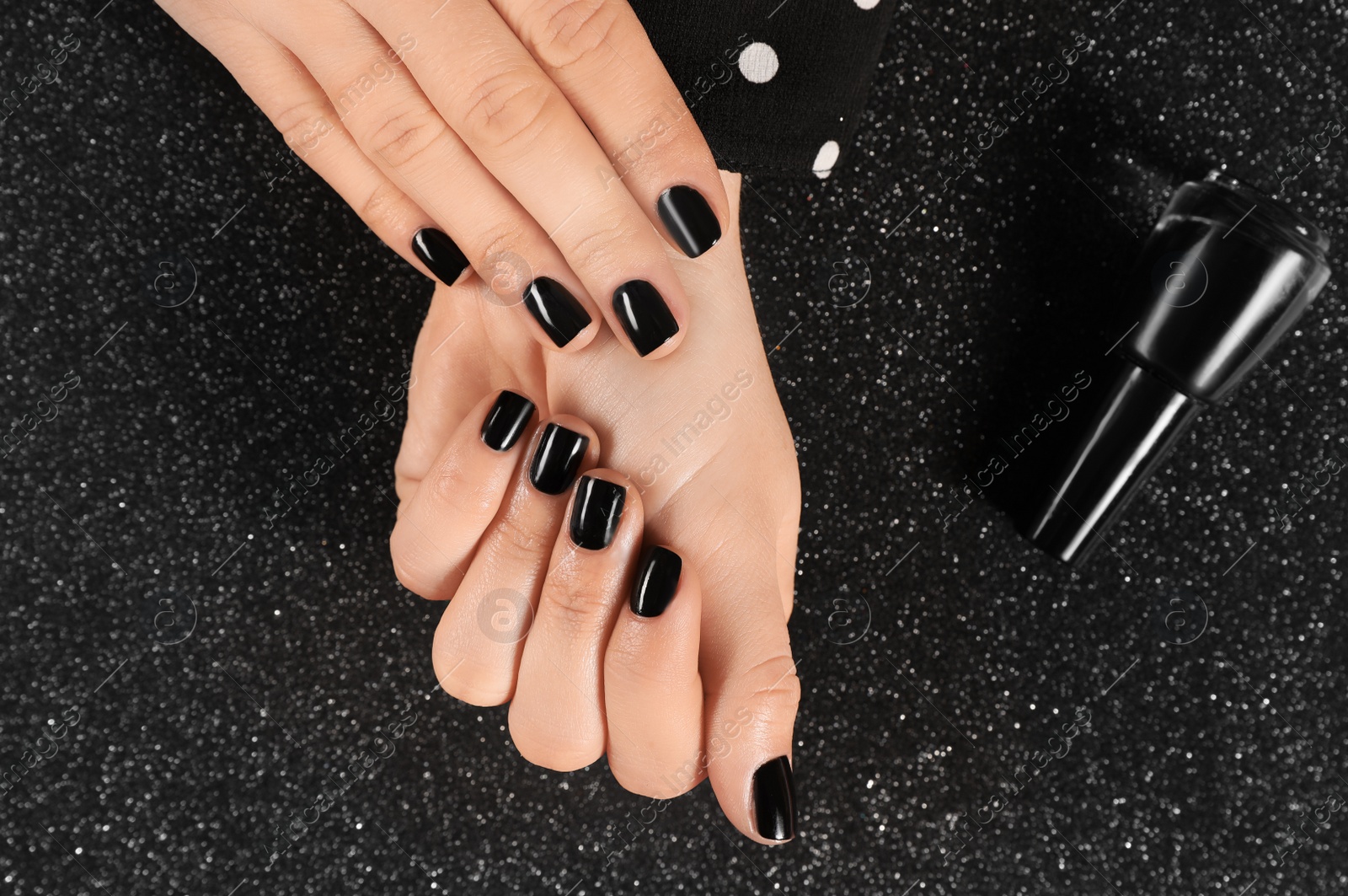 Photo of Woman with black manicure and nail polish bottle on dark background, top view