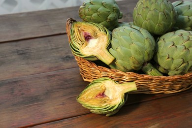 Photo of Wicker basket with fresh raw artichokes on wooden table. Space for text