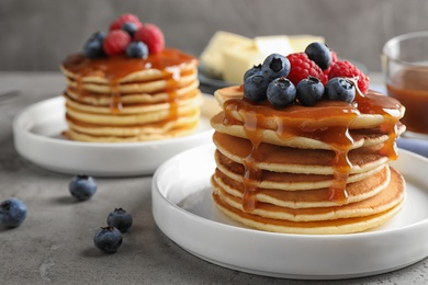 Delicious pancakes with fresh berries and syrup on grey table