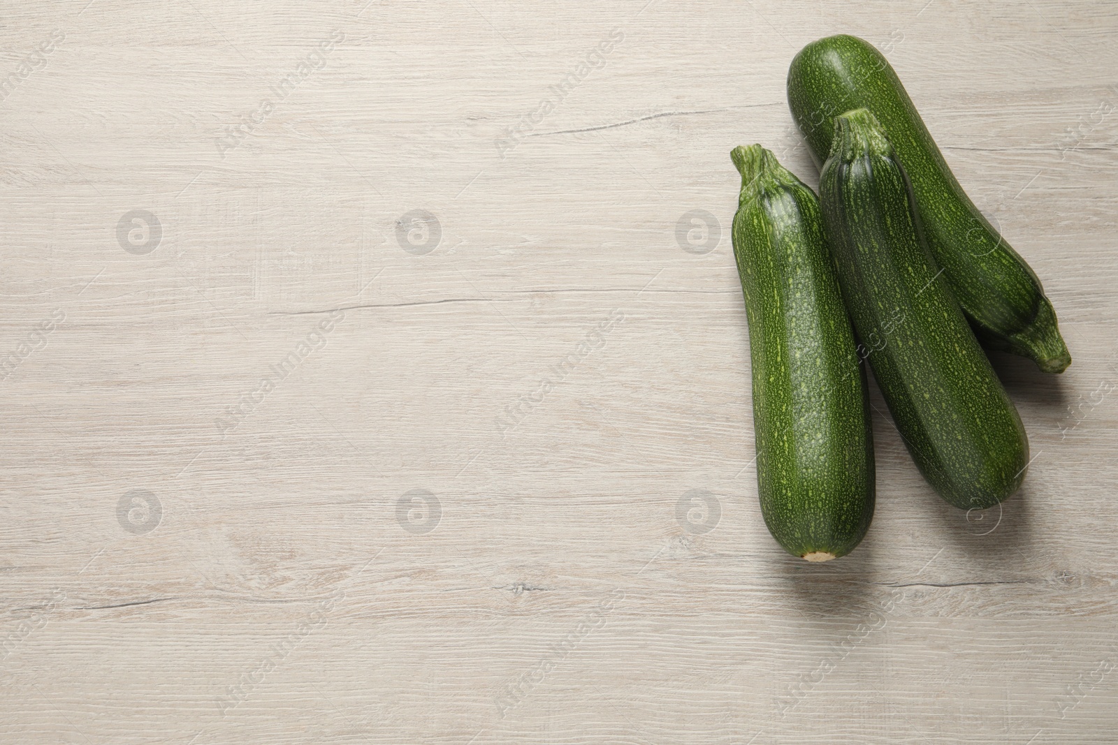 Photo of Raw ripe zucchinis on white wooden table, flat lay. Space for text