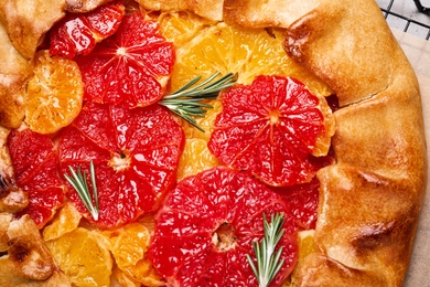 Photo of Tasty galette with citrus fruits and rosemary on table, top view