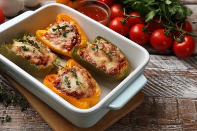 Photo of Tasty stuffed peppers in dish and ingredients on wooden table