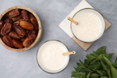 Glasses of delicious date smoothie, dried fruits and mint on light grey table, flat lay